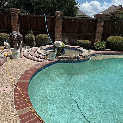 Two workers are repairing or maintaining a hot tub beside a backyard swimming pool on a sunny day. Tools and buckets are scattered around the area.