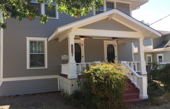 A two-story gray house with white trim, a small covered front porch, dual front doors, red steps, and a bush in front—perfect inspiration for home renovations North Texas residents will love.