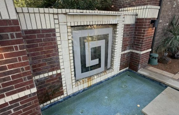 A square-patterned water feature set in a brick wall flows into a small blue-tiled pool with concrete stepping stones, creating a stylish retreat perfect for outdoor living spaces in North Texas.